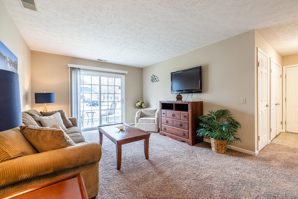 Carpeted living room with sliding glass door access to our door patio or deck of apartment model.