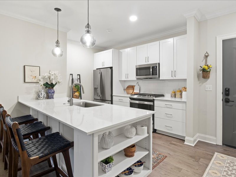 A kitchen with white cabinets, stainless steel appliances, and white granite countertop with extra seating at the breakfast bar.