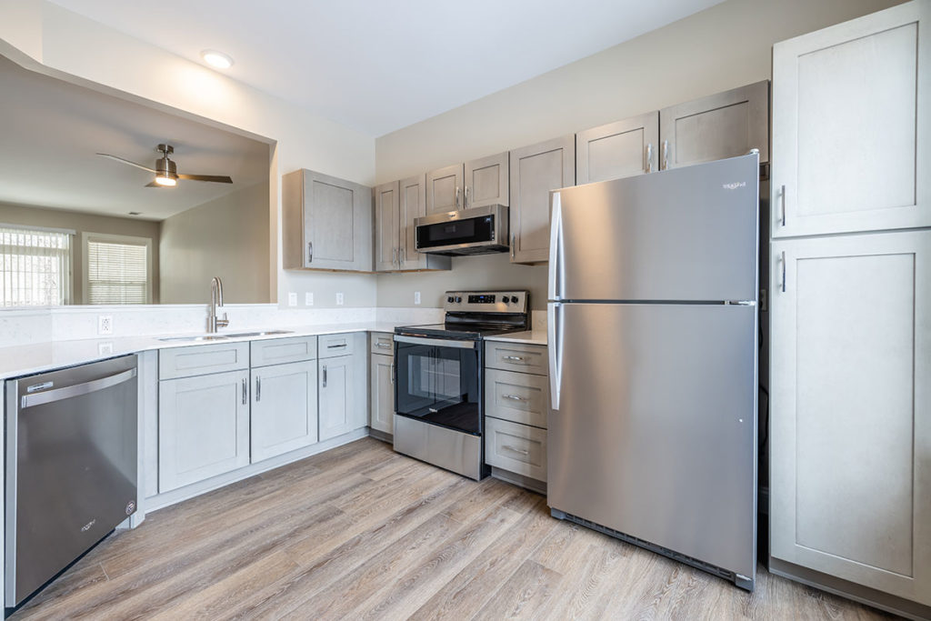 View of the renovated Townhome kitchen with stainless steel appliances, wood look vinyl plank flooring, gray cabinetry and white quartz contertops.