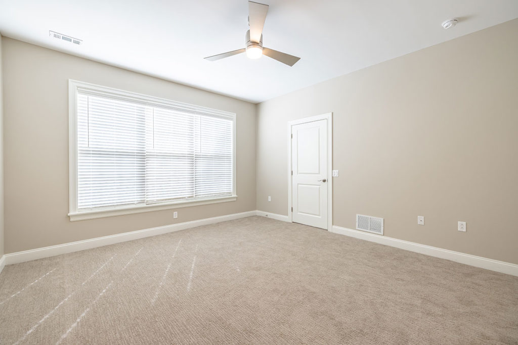 Carpeted master bedroom view with ceiling fan and access to walk-in closet