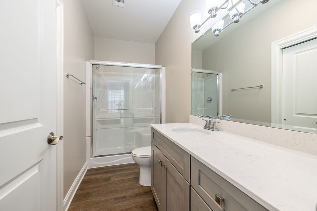 View of the renovated master bathroom with walk-in shower and new vanity with white quartz countertop and vinyl plank flooring