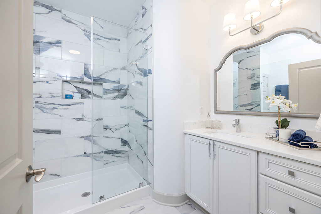 Master bathroom with porcelain tile flooring and shower walls with white single vanity and quartz countertops.
