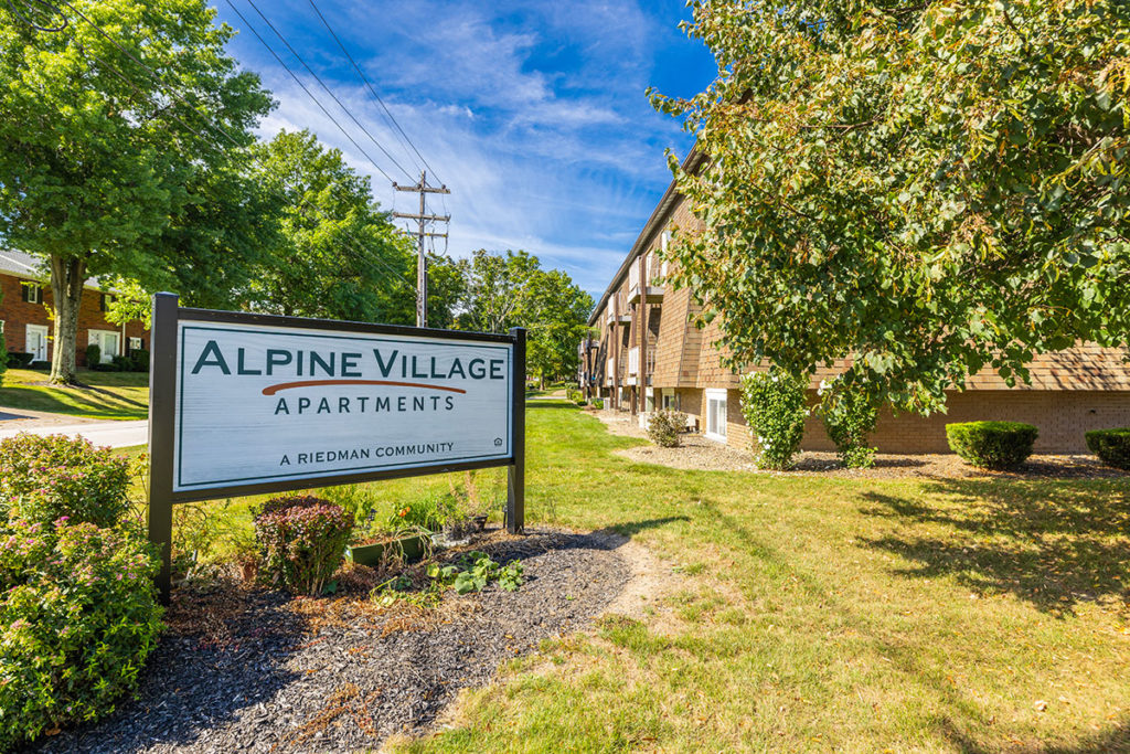 Alpine Village Apartments sign, and entrance leading into community