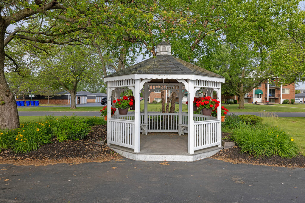 White gazebo surrounded by lush greenery and colorful flowers. Inside, a cozy seating area awaits, providing a tranquil space to relax and take in the surrounding beauty. The gazebo's small size lends an intimate and charming atmosphere, perfect for private conversations or enjoying moments of solitude.