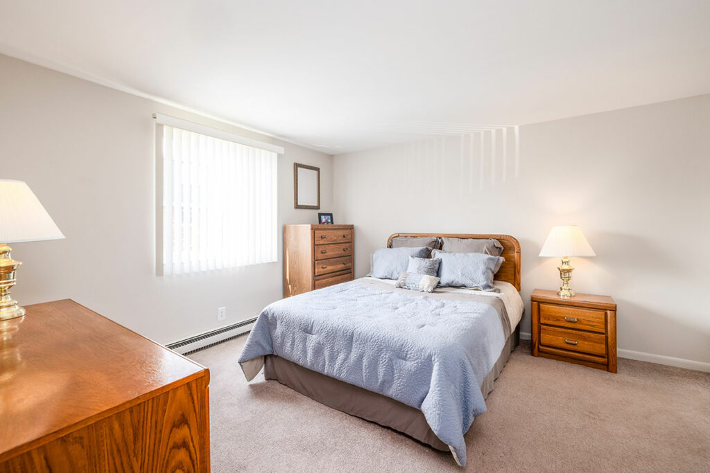 A comfortable bed occupies the center of the room, dressed with inviting bedding and decorative pillows. Adjacent to the bed, a nightstand with a bedside lamp provides convenient lighting for nighttime reading or relaxation.