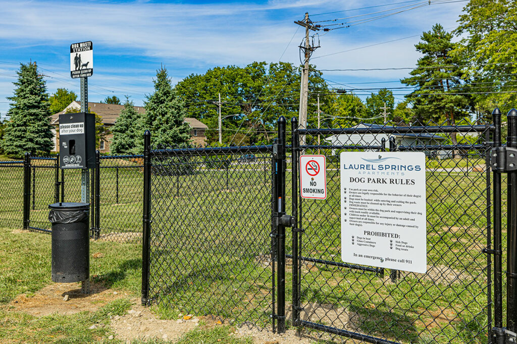 Image of the entrance to the designated dog park area, featuring posted dog park rules for residents to follow. Adjacent to the rules signage, there is a dog waste station for convenient disposal of pet waste.